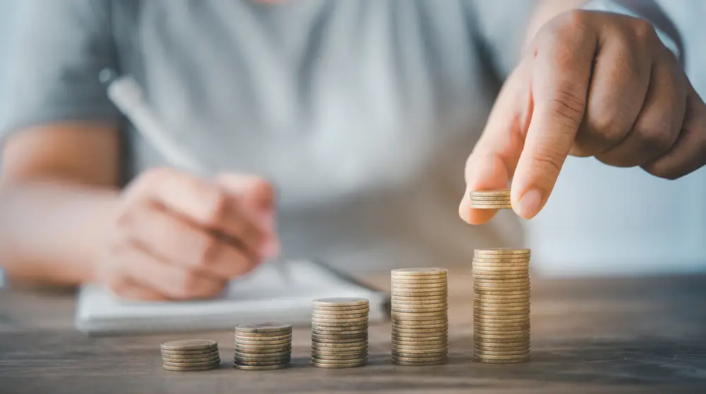 Darowizna dla fundacji a podatek – monety ułożone w słupki różnej wysokości, w tle mężczyzna dokonujący obliczeń – fundacjaktos.pl